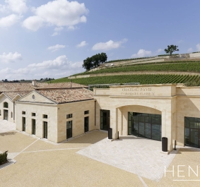 Helles Gebäude mit Bögen, umgeben von Weinbergen und blauem Himmel.