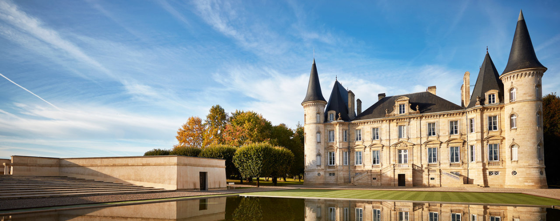 Schloss mit Türmen spiegelt sich in ruhigem Wasser, umgeben von herbstlichen Bäumen.