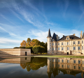 Schloss mit Türmen spiegelt sich in ruhigem Wasser, umgeben von herbstlichen Bäumen.