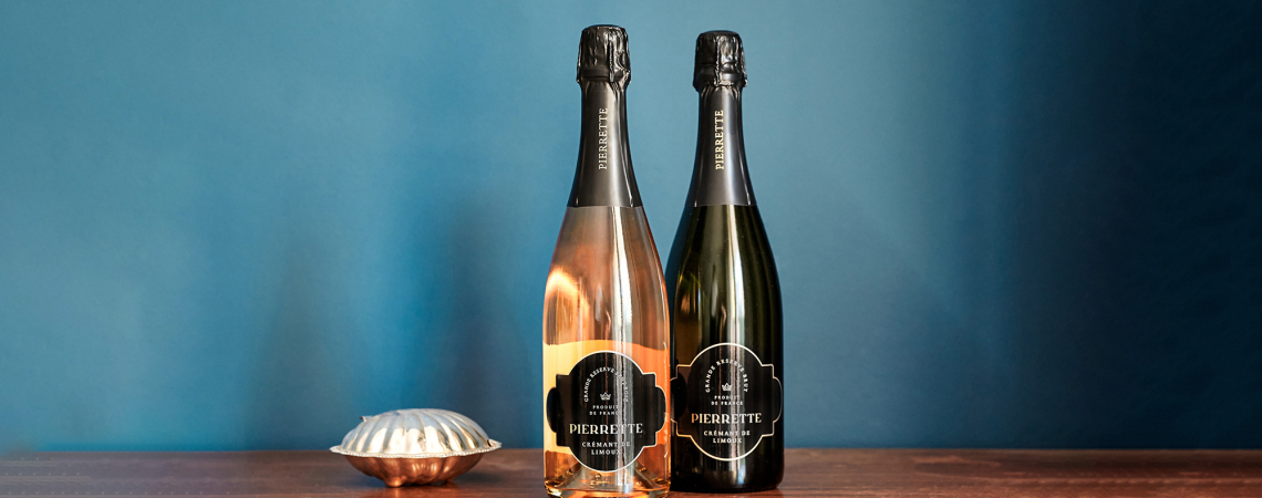 Zwei Champagnerflaschen auf Holzuntergrund vor blauem Hintergrund, links Schale.