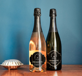 Zwei Champagnerflaschen auf Holzuntergrund vor blauem Hintergrund, links Schale.