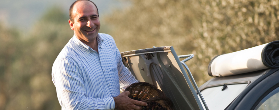 Mann mit Korb voller Oliven, steht neben einem Auto im Freien.