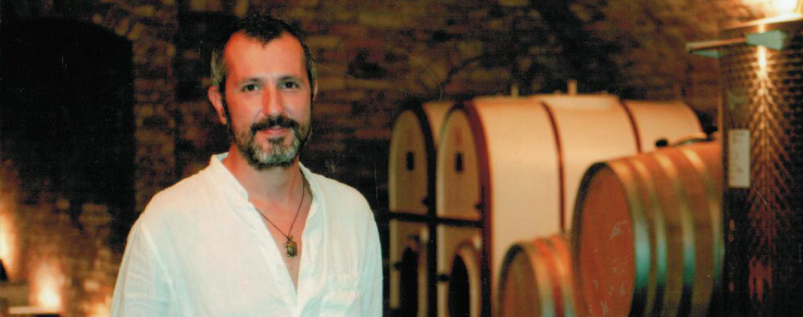 Mann in weißem Hemd steht in einem stimmungsvollen Weinkeller vor Fässern.