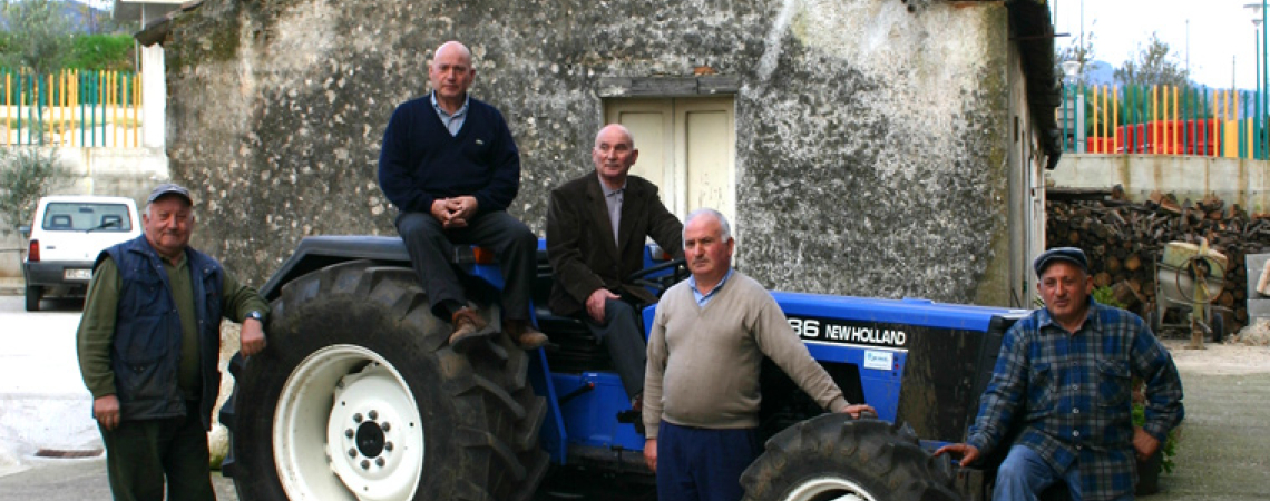 Fünf Männer posieren neben und auf einem blauen Traktor vor rustikaler Wand.