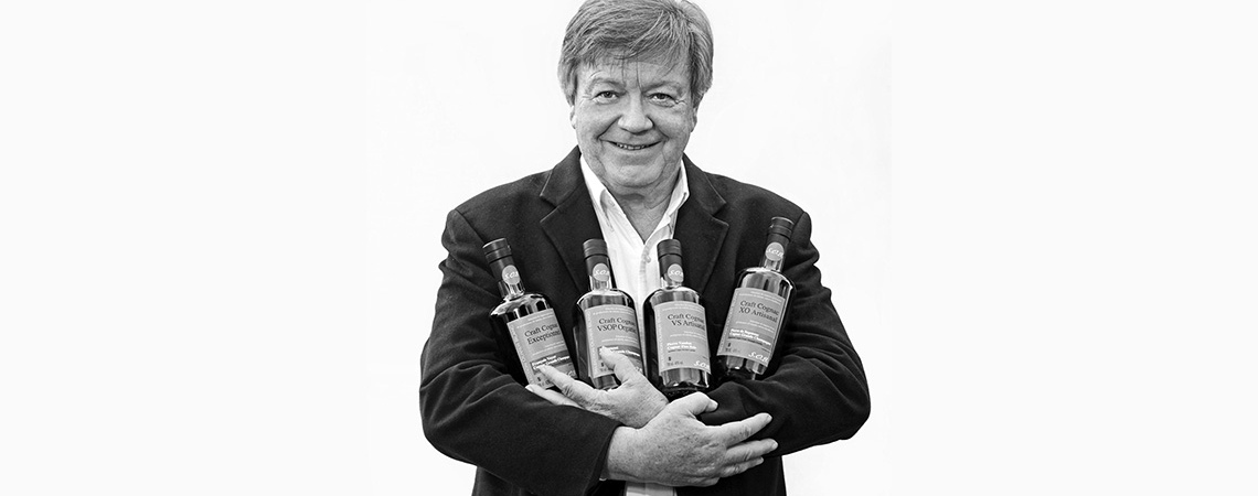 Mann in Anzug hält vier Flaschen Alkohol lächelnd im Arm.