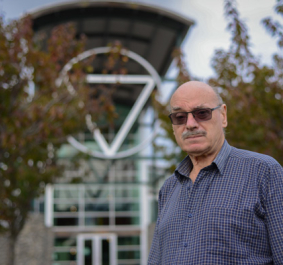 Mann mit Brille vor moderner Gebäudefassade, umgeben von Bäumen.