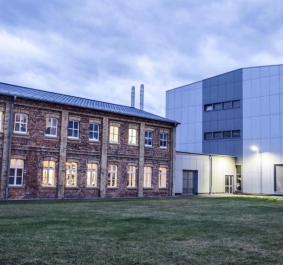 Altes Backsteingebäude neben modernem Anbau bei Abenddämmerung.