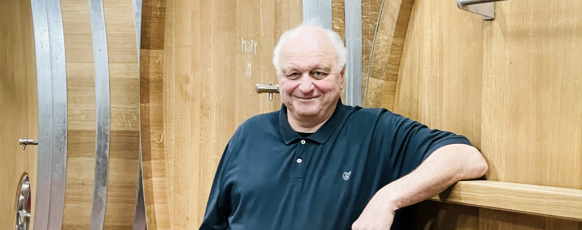 Mann in dunklem Poloshirt vor großen Holzfässern.