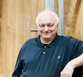 Mann in dunklem Poloshirt vor großen Holzfässern.