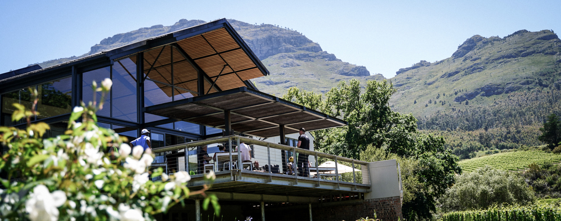 Modernes Gebäude mit Glasfassade, Bergkulisse und üppiger Vegetation im Hintergrund.