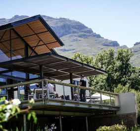 Modernes Gebäude mit Glasfassade, Bergkulisse und üppiger Vegetation im Hintergrund.