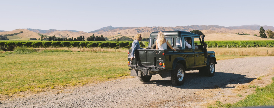 Geländewagen auf Schotterstraße in idyllischer Hügellandschaft bei klarem, blauem Himmel.