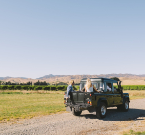 Geländewagen auf Schotterstraße in idyllischer Hügellandschaft bei klarem, blauem Himmel.