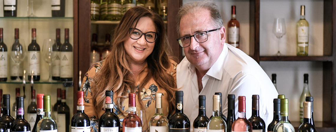 Zwei Personen hinter einer Theke mit einer Auswahl an Weinflaschen.