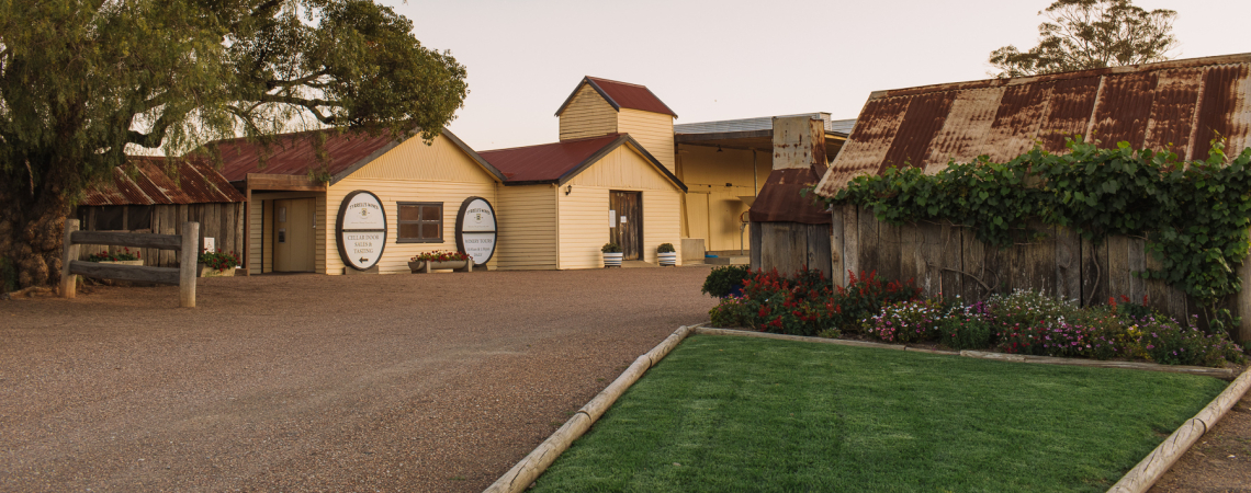 Hof mit gelbem Gebäude, rostigem Dach und gepflegtem Garten im Abendlicht.