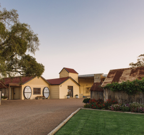 Hof mit gelbem Gebäude, rostigem Dach und gepflegtem Garten im Abendlicht.