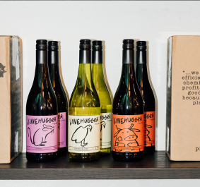 Weinflaschen mit bunten Etiketten und Pappkartons auf einem Regal.