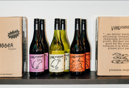 Weinflaschen mit bunten Etiketten und Pappkartons auf einem Regal.