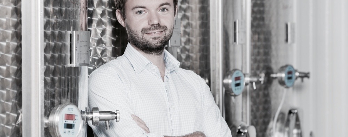 Mann mit Hemd vor großen Metalltanks in industriellem Umfeld.