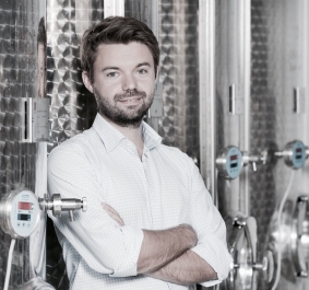 Mann mit Hemd vor großen Metalltanks in industriellem Umfeld.