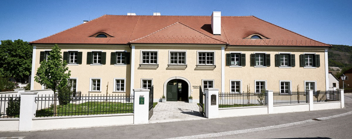 Gelbes, historisches Gebäude mit roten Dachziegeln und grünen Fensterläden.