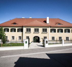Gelbes, historisches Gebäude mit roten Dachziegeln und grünen Fensterläden.