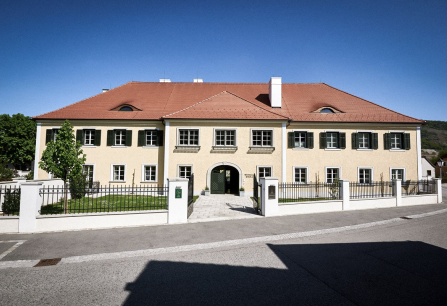 Gelbes, historisches Gebäude mit roten Dachziegeln und grünen Fensterläden.