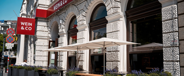 Historische Fassade mit eleganten Bögen, Terrassenbereich und sonnengeschütztem Sitzbereich.