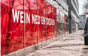 Rotes Schaufenster mit modernem Schriftzug an einem Bürogebäude entlang eines Gehwegs.