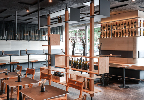 Modernes Restaurant mit Holzmöbeln, minimalistischen Regalen und dekorativen Weinflaschen.