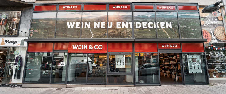 Moderne Fassade eines Weinladens mit großen Glasfenstern und rotem Logo-Element.