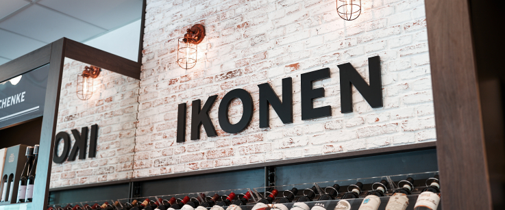 Weinregal mit schwarzem Schriftzug auf weißer Ziegelwand und hängenden Wandlampen.