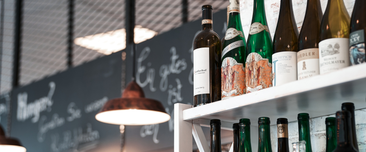 Weinflaschen auf einem weißen Regal vor einer Ziegelwand mit dekorativen Lampen.