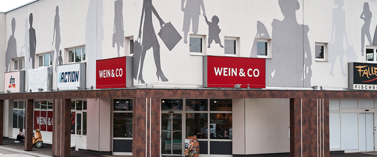 Großes Gebäude mit Silhouetten und verschiedenen Ladenschildern, moderne Fassadenoptik.