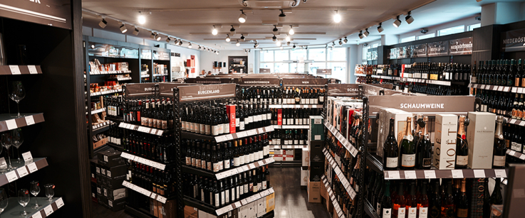 Gut beleuchteter Wein- und Spirituosenladen mit Regalen voller Flaschen und Gläser.