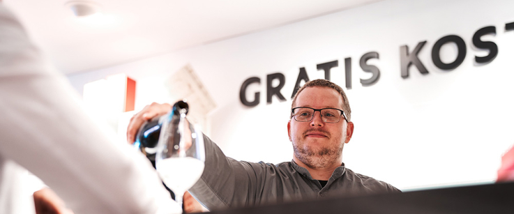 Mann schenkt Getränk in Glas hinter schwarzem Tresen ein.