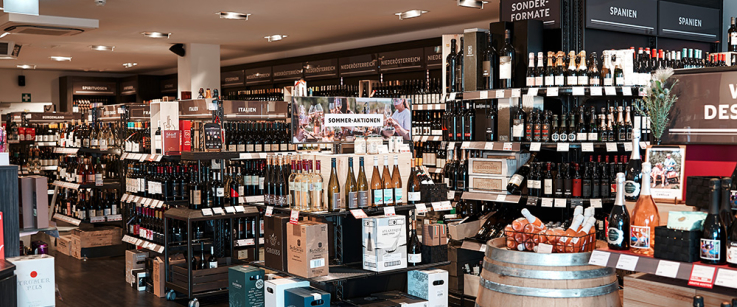 Weinladen mit zahlreichen Flaschen auf Regalen und einem hölzernen Weinfass.