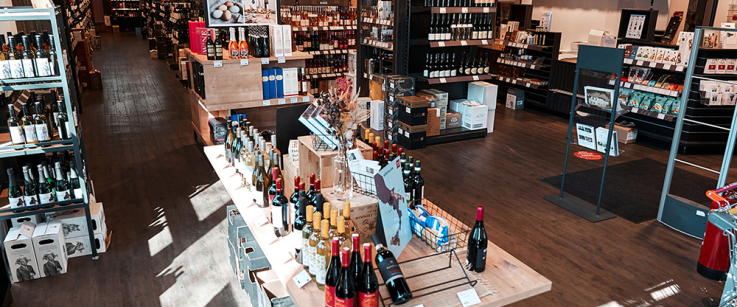 Heller Weinladen mit Holzböden, mehreren Weinregalen und moderner Produktpräsentation.