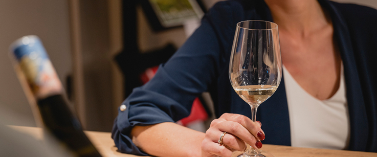 Frau mit Weinglas lächelt an einer Theke.