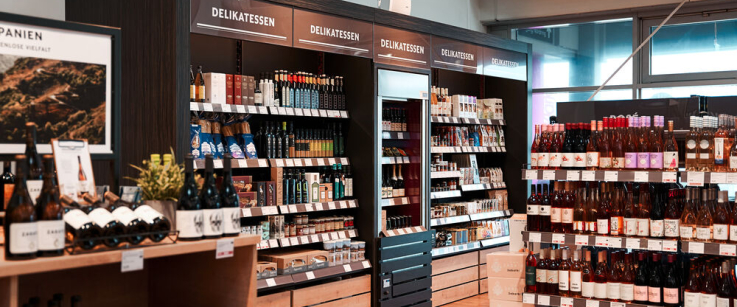 Moderner Feinkostladen mit Regalreihen voller Weinflaschen und Gourmet-Produkten.
