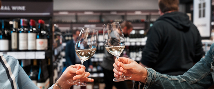 Zwei Personen stoßen mit Weingläsern in einem Weinladen an.