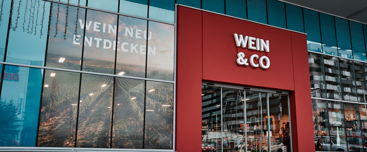 Moderne Glasfassade mit Weinmotiv und rotem Eingang.