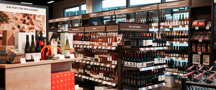 Moderner Weinladen mit Weinflaschen, festlicher Präsentationstisch und Einkaufswagen im Vordergrund.