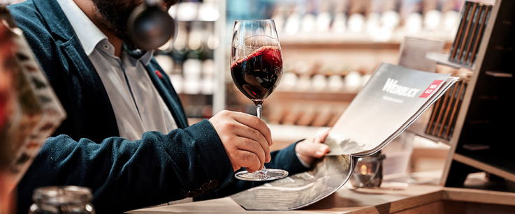 Mann in Anzug genießt Rotwein an der Bar, liest Magazin.