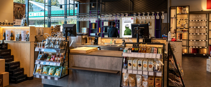 Moderner Kassenbereich mit Regal, hängenden Gläsern und beleuchteten Holzdetails im Verkaufsraum.