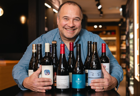 Mann in blauem Hemd präsentiert eine Auswahl verschiedener Weinflaschen in modernem Geschäft.