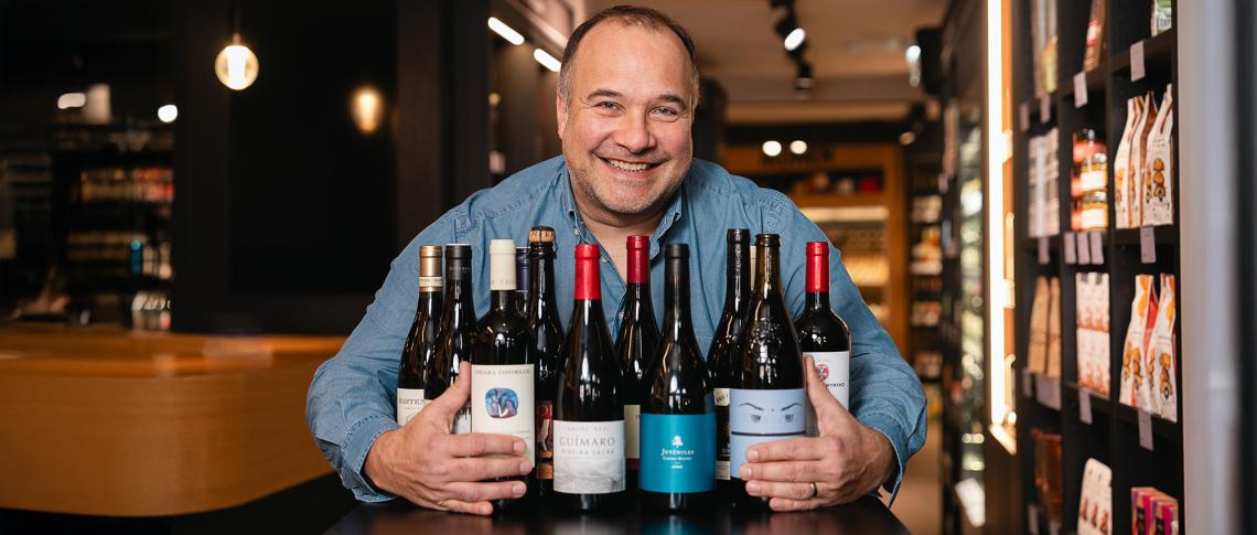 Mann in blauem Hemd präsentiert eine Auswahl verschiedener Weinflaschen in modernem Geschäft.