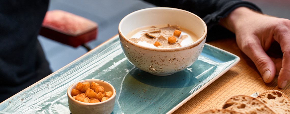 Keramikschale mit Suppe und kleinen Croutons auf stilvollem, türkisem Teller.