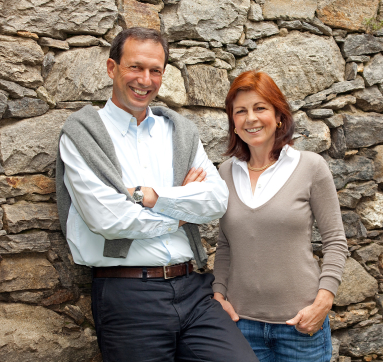 Zwei Personen lächelnd vor einer rustikalen Steinmauer.