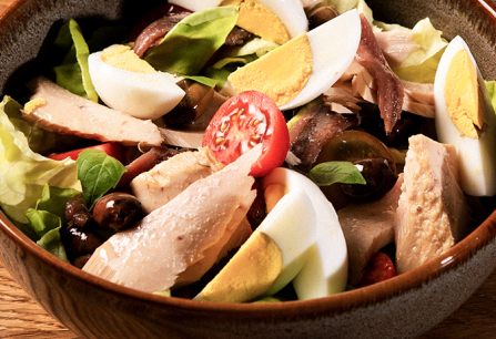 Frischer Salat mit Eiern, Hühnchen, Tomaten und Oliven in einer Keramikschüssel.